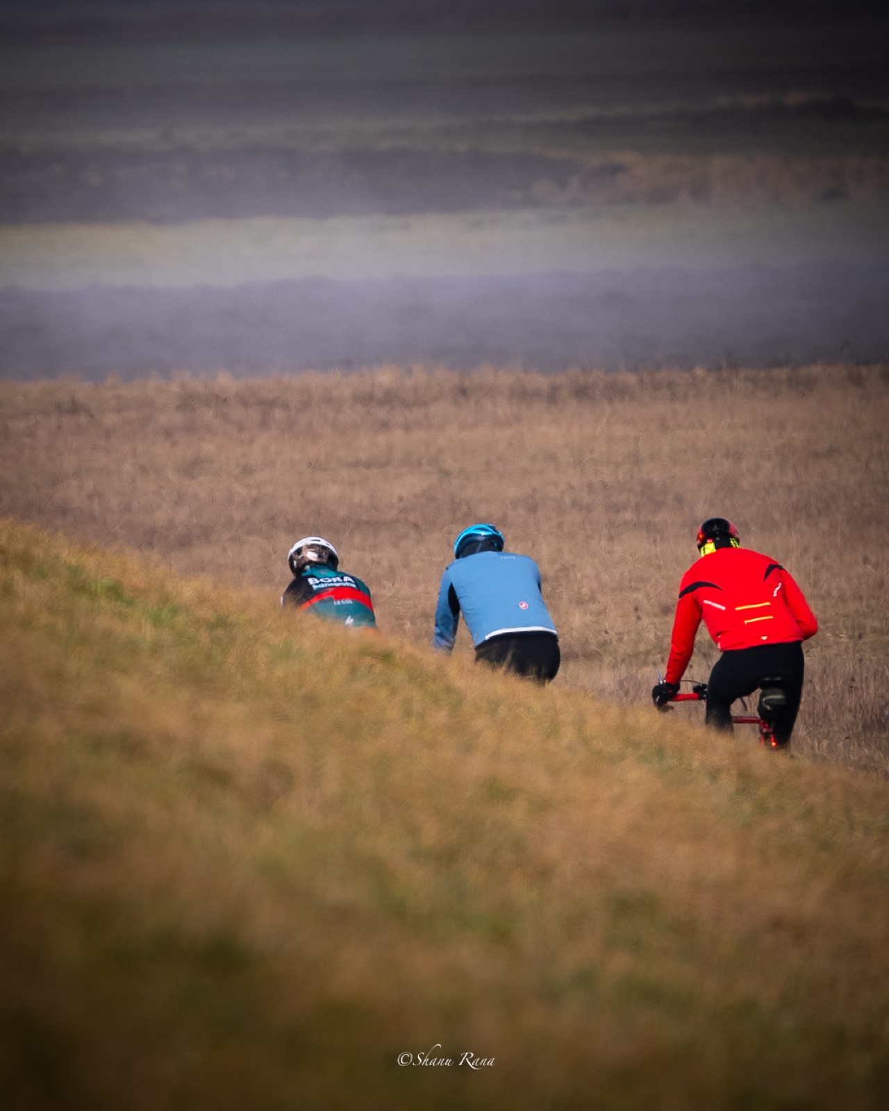 Three cyclists riding along a grassy dyke