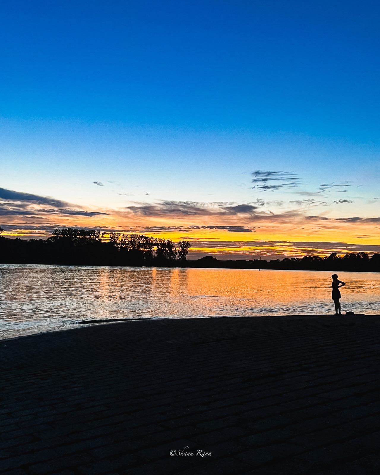 Person silhouetted at the edge of a lake after sunset