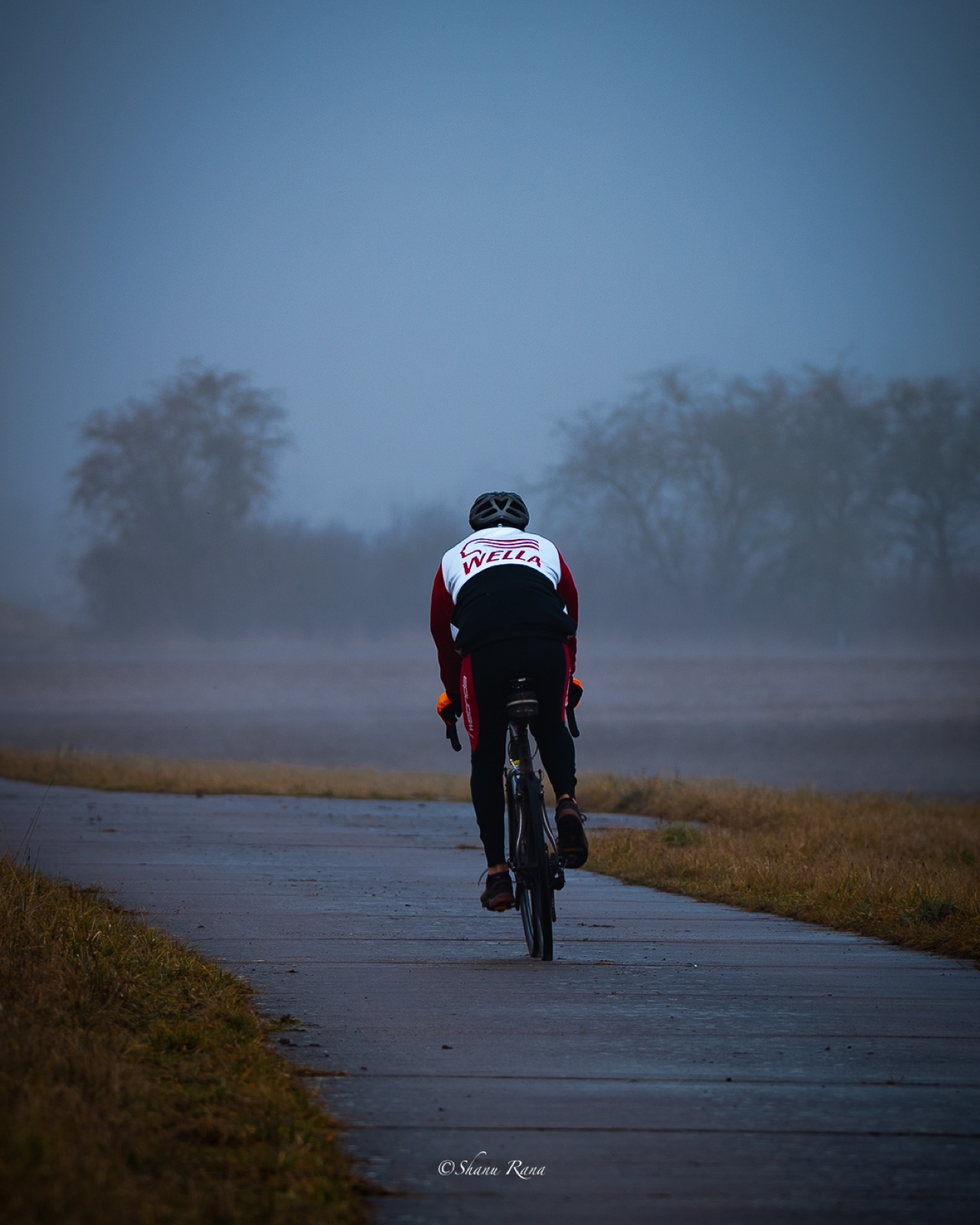 Road cyclist riding into thick morning fog