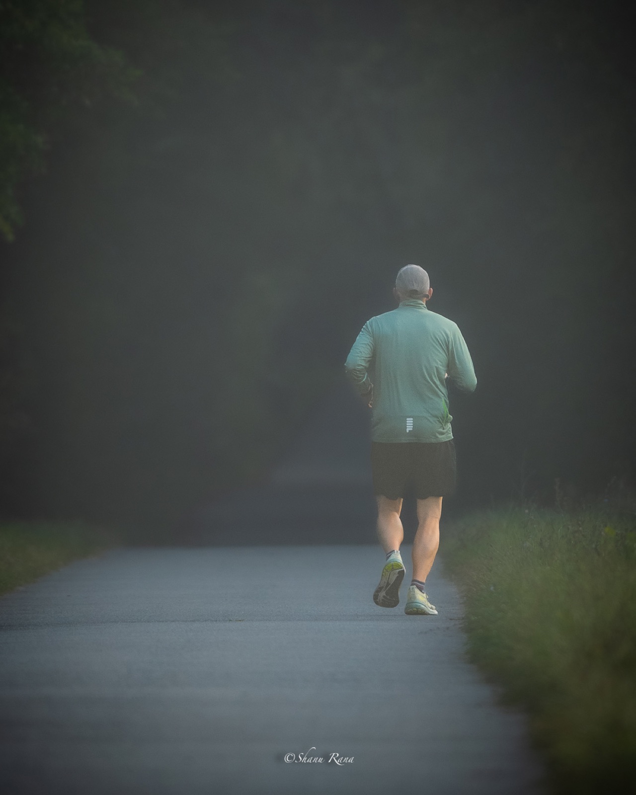 Runner disappearing into morning fog on a straight road